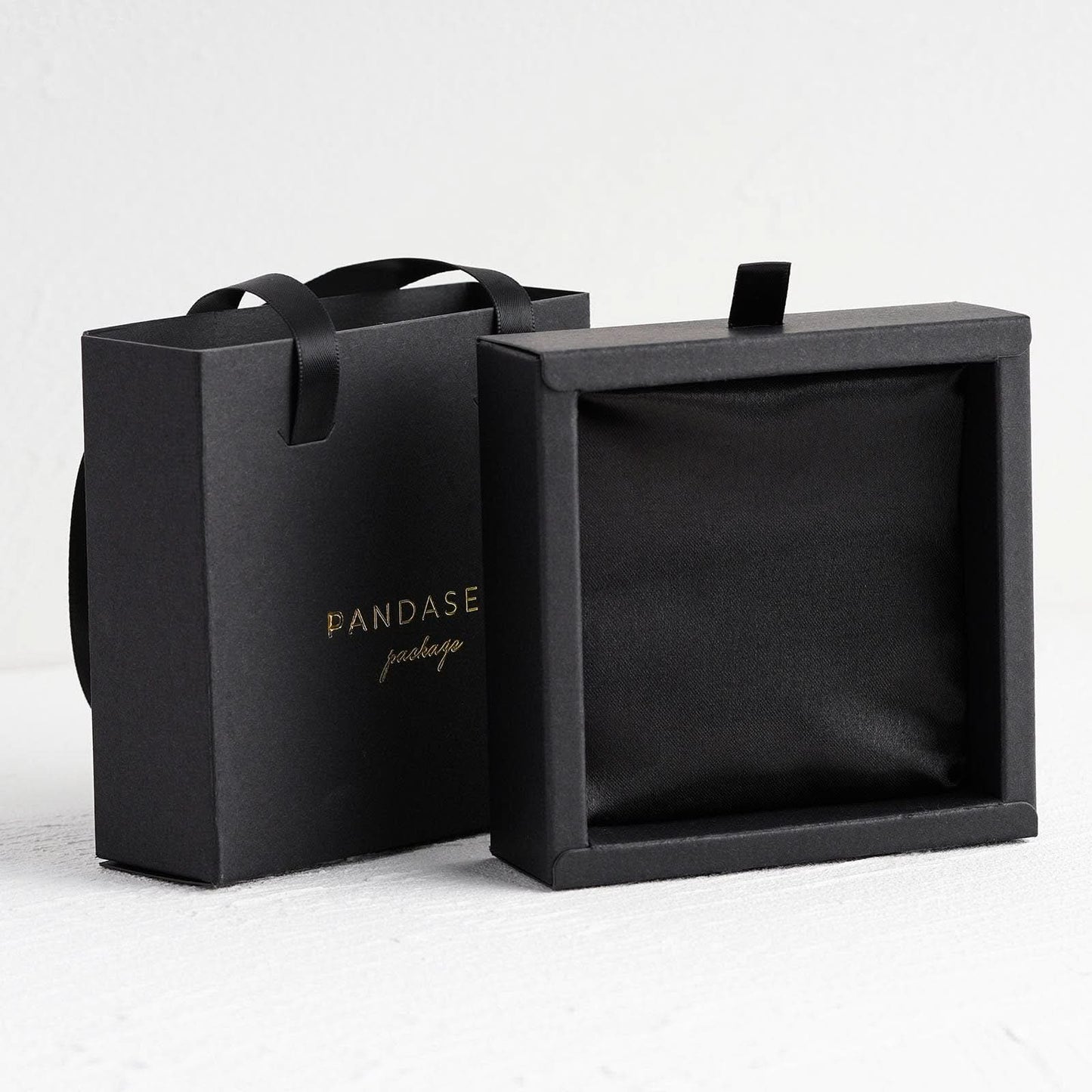Black jewelry paper box with satin sponge inside. Gold logo is debossed on the front side.