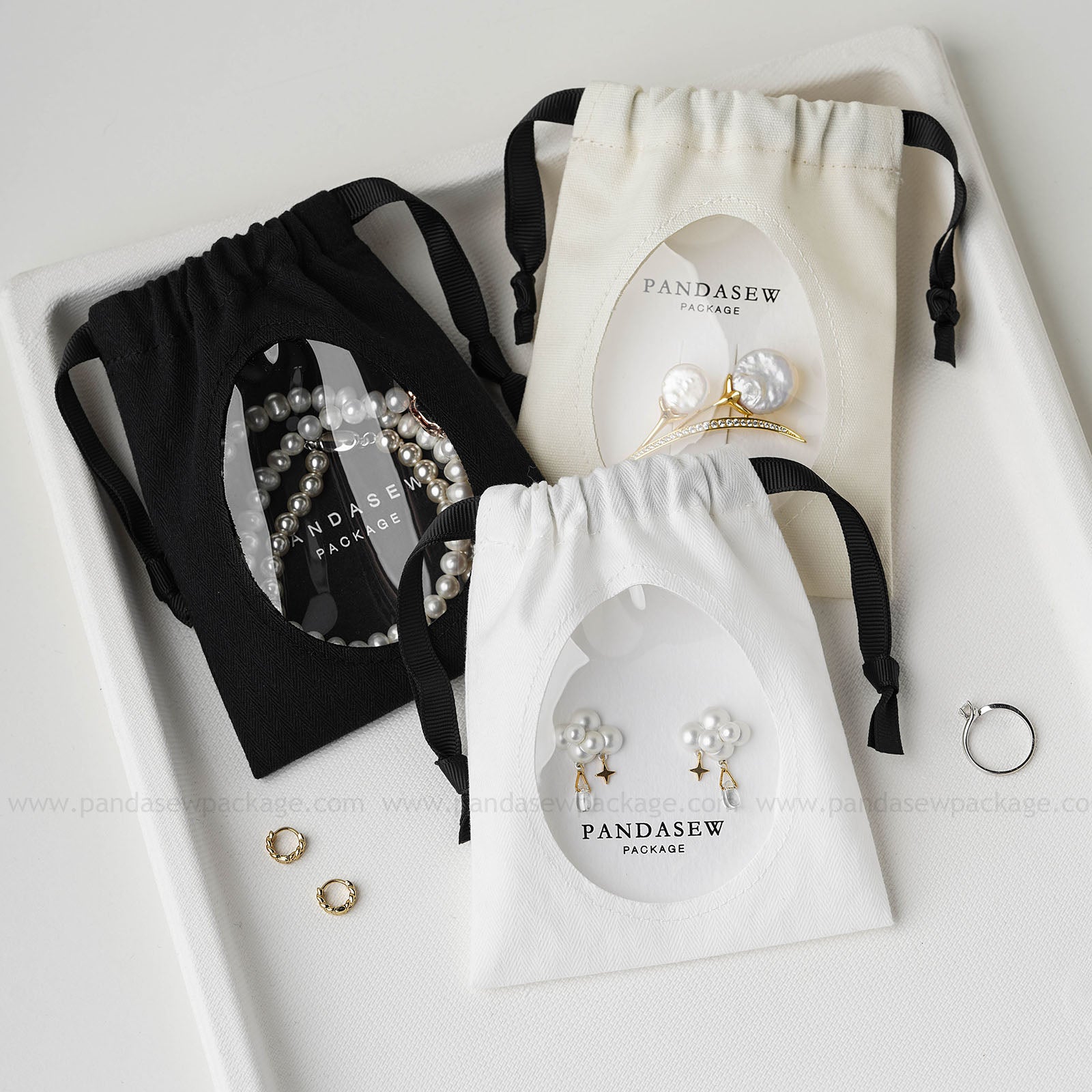Pandasew custom logo cotton jewelry drawstring bags with transparent window displaying earrings and bracelet in black, white, and beige.
