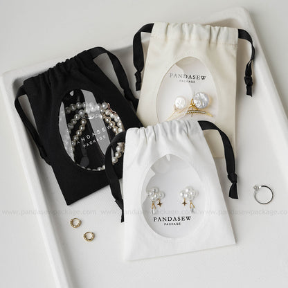 Pandasew custom logo cotton jewelry drawstring bags with transparent window displaying earrings and bracelet in black, white, and beige.