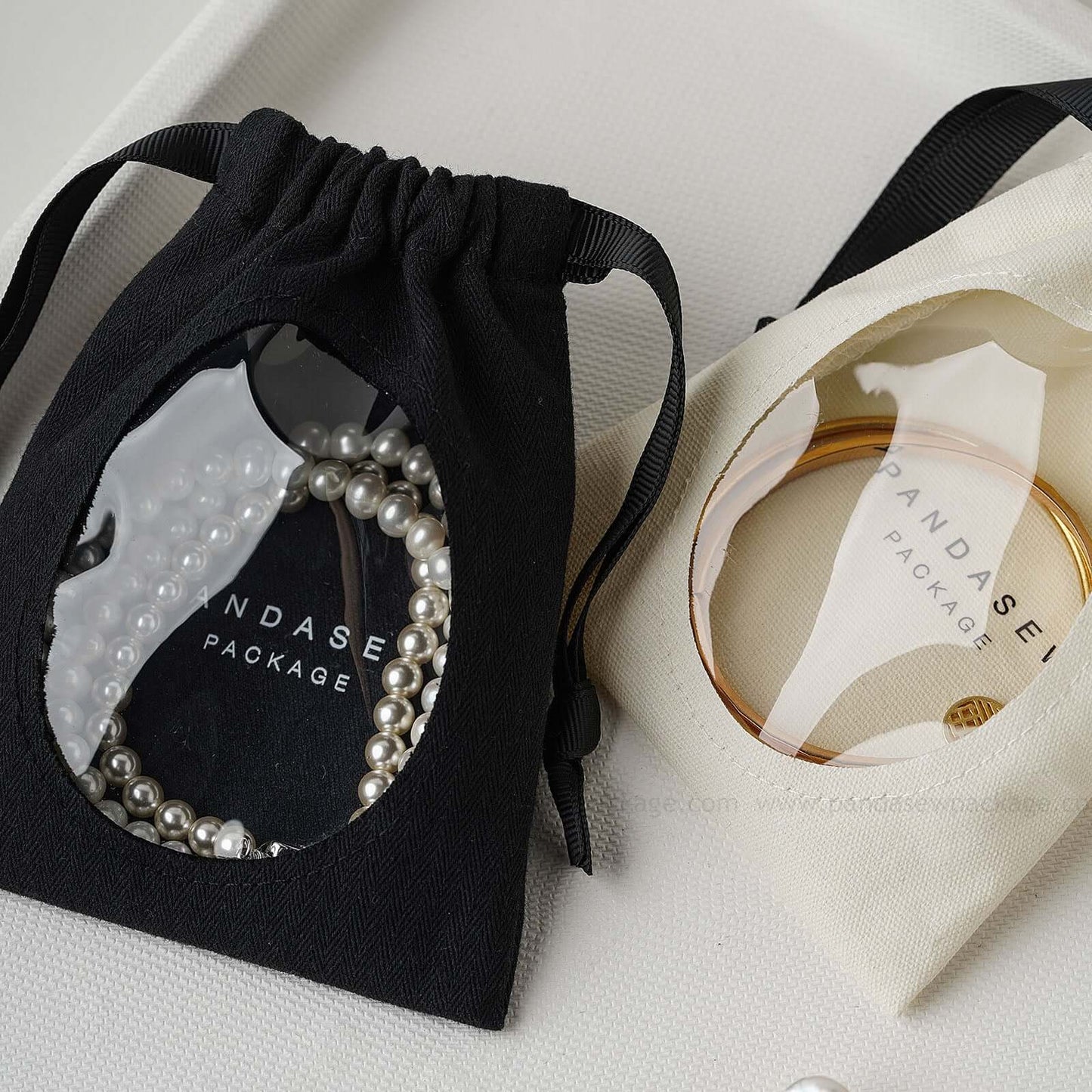 Cotton jewelry drawstring bags with transparent windows showcasing pearl and bracelet contents, eco-friendly and customizable.