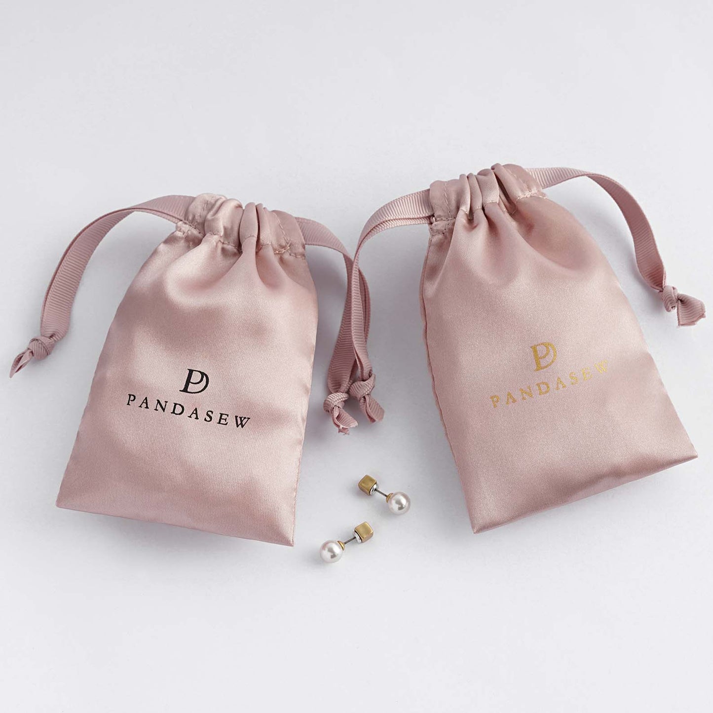 pink color satin bag with black smooth satin string, black logo on pink satin, hair, candles, soap packaging